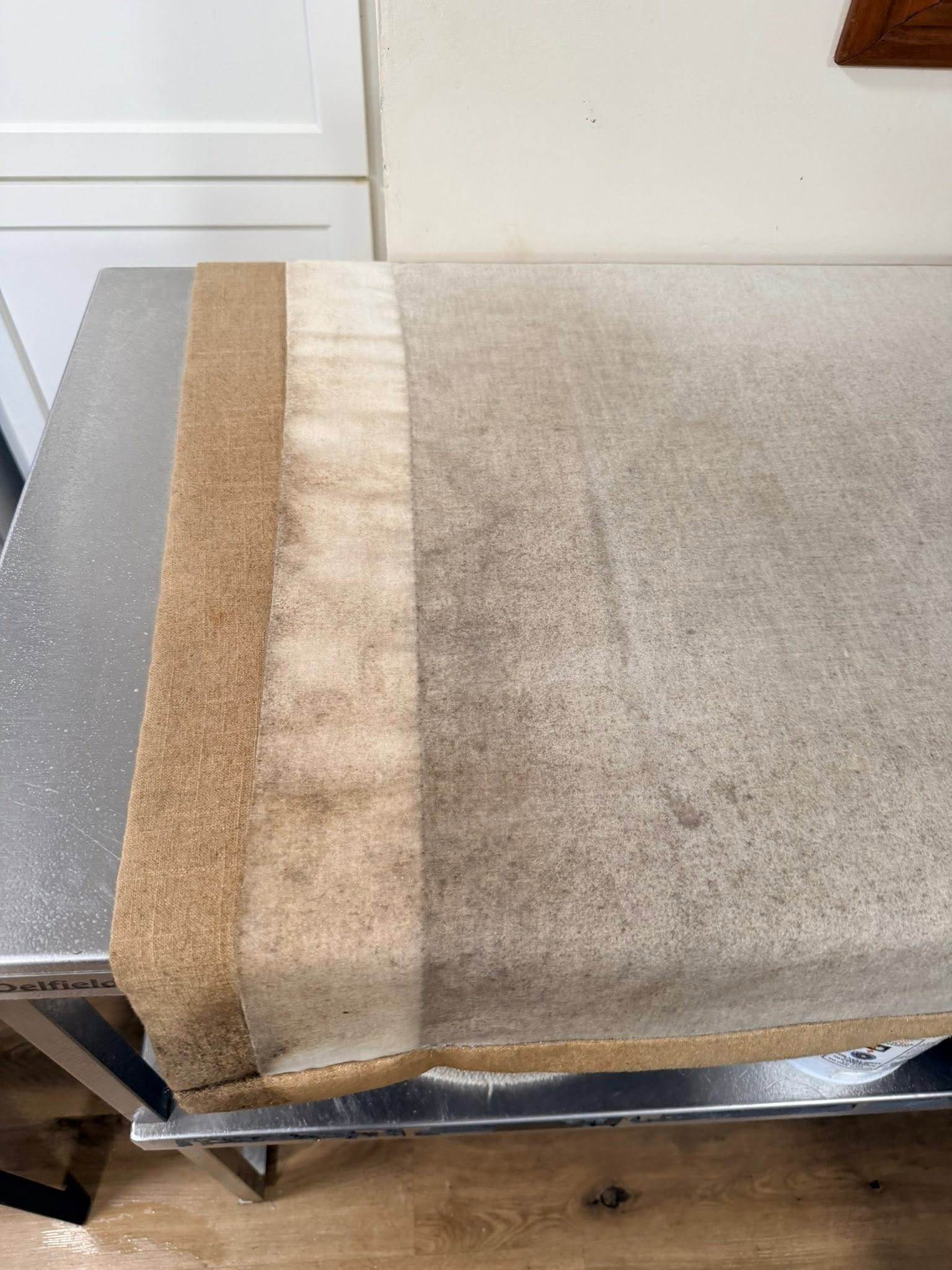 A drape laid across a table, partly cleaned, with the cleaned strip clearly lighter than the dirty fabric