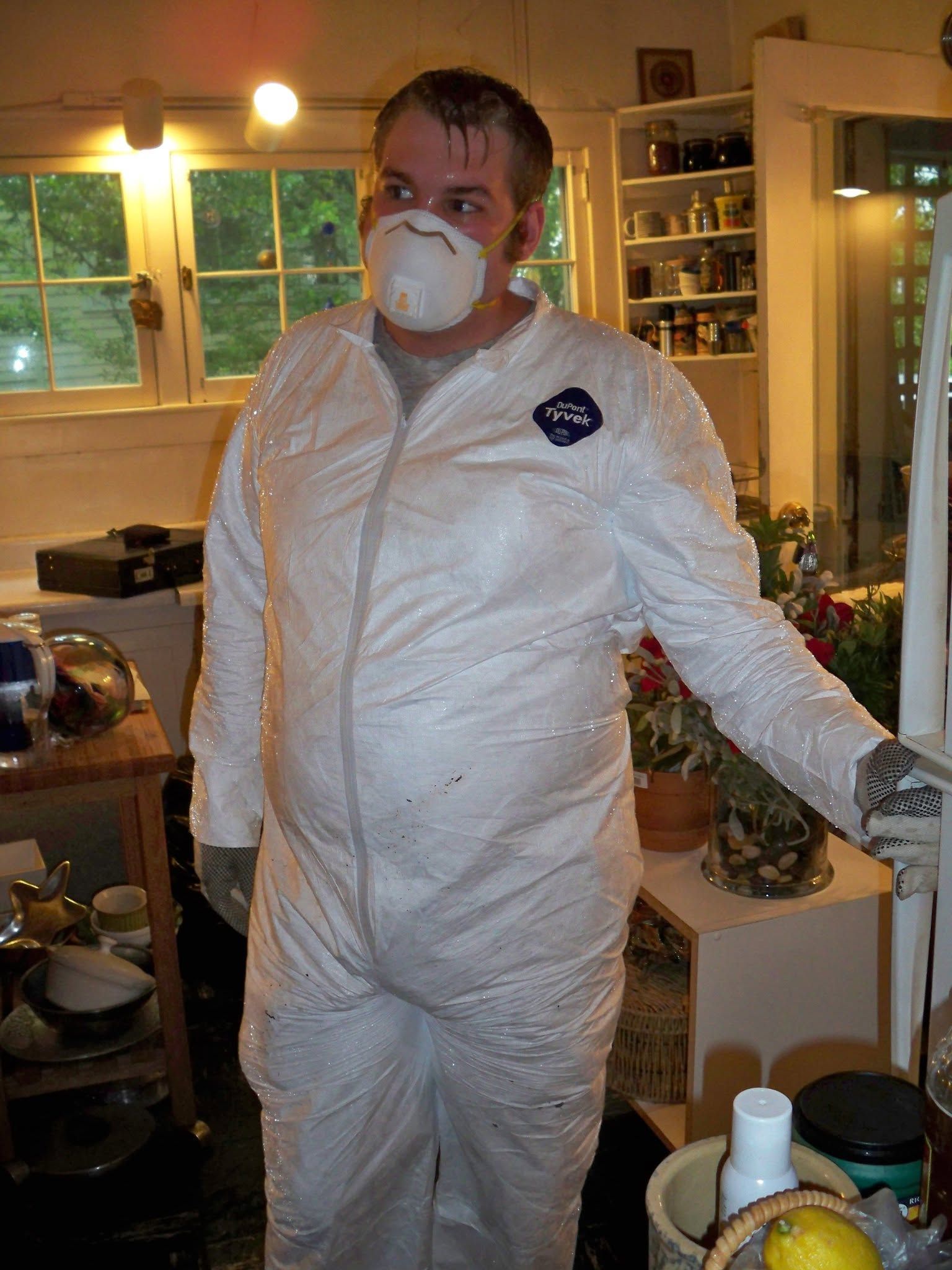 Elijah Burr in a white protective suit and respirator mask, standing in a kitchen on a restoration job