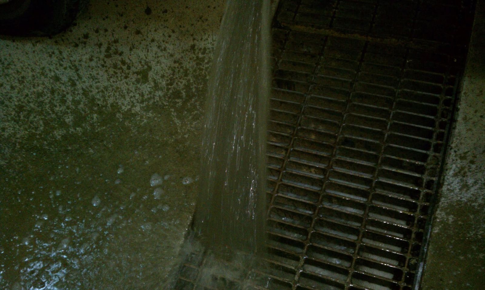 Water running down into a dark crawlspace beside a drain grate