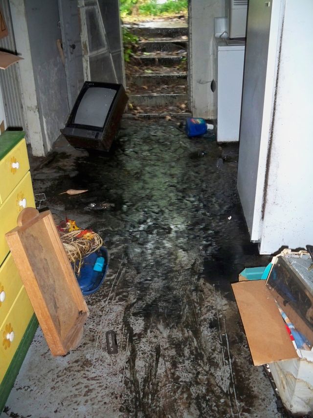 Flooded basement hallway with debris, stairs at the back