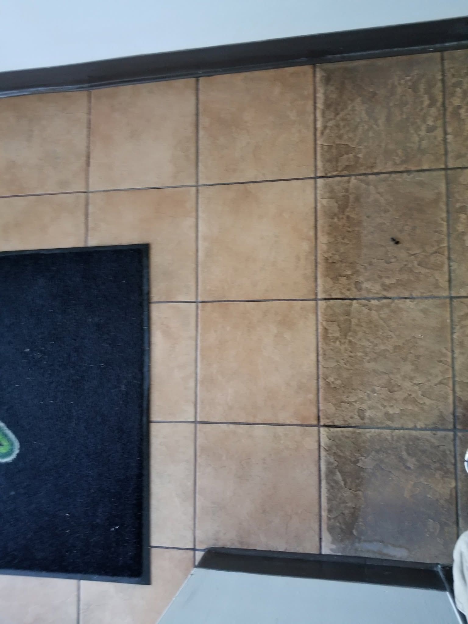 A tile floor with a doormat, part of the floor lighter than the rest